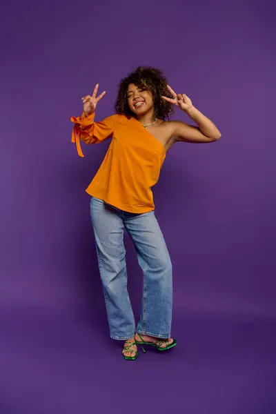African American woman in stylish attire posing with peace sign against vibrant backdrop. — Stock Photo