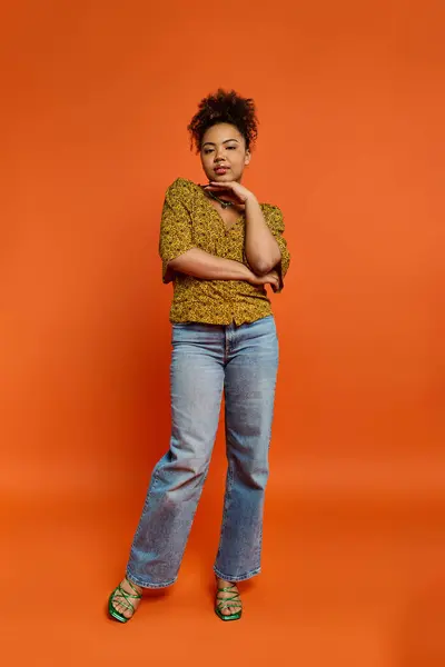 Elegante donna afroamericana in posa di fronte a un vivace sfondo arancione. — Foto stock