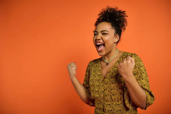 A beautiful African American woman with an open mouth, posing against a vibrant orange backdrop. — Stock Photo