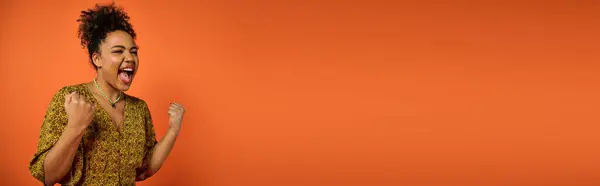 Elegante donna afroamericana si erge con la bocca aperta sullo sfondo arancione. — Foto stock