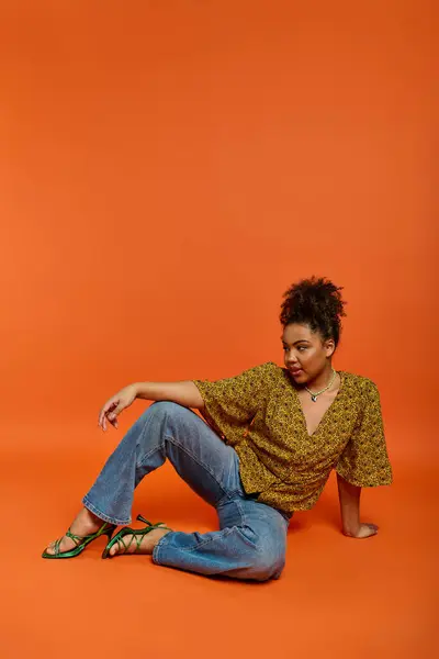 Une femme afro-américaine en tenue élégante s'assoit les jambes croisées sur le sol, exsudant une grâce sereine. — Photo de stock