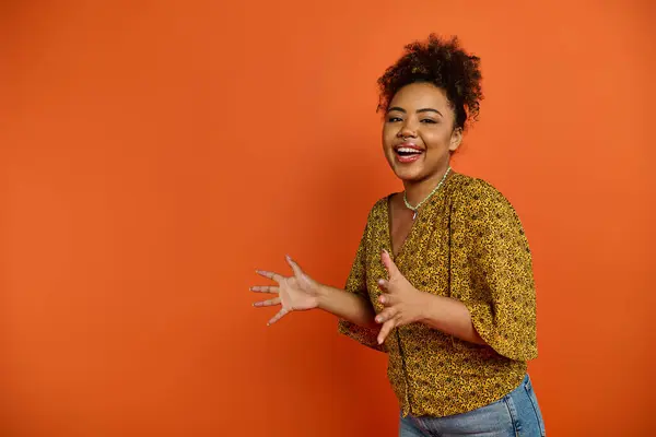 African American woman smiling, hands outstretched in stylish attire against vibrant backdrop. — Stock Photo