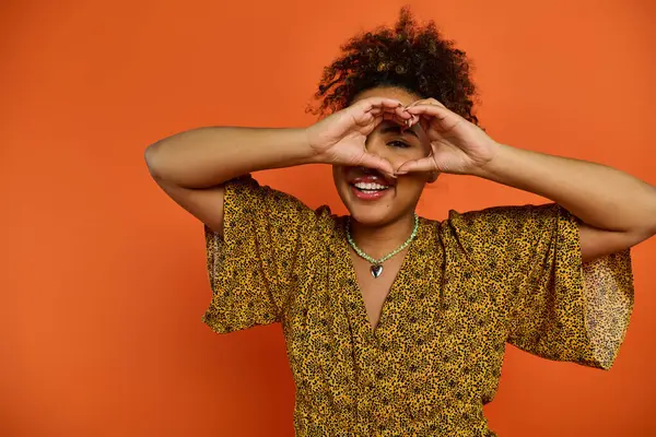 African American woman in stylish attire creating a heart shape with her hands. — Stock Photo