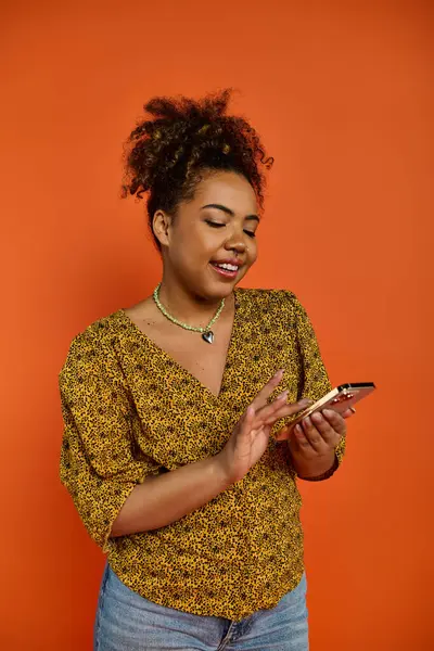 African American woman in yellow top looking at cell phone, vibrant backdrop. — Stock Photo