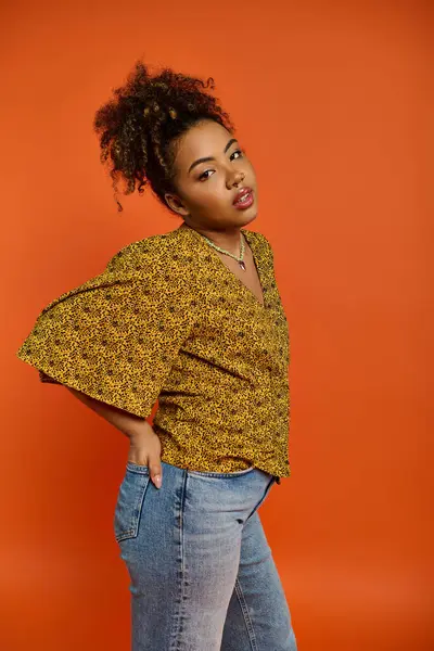 Elegant African American woman poses in stylish attire against vibrant orange backdrop. — Stock Photo