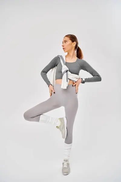 A sporty young woman wearing gray and white activewear poses on a grey background. — Stock Photo