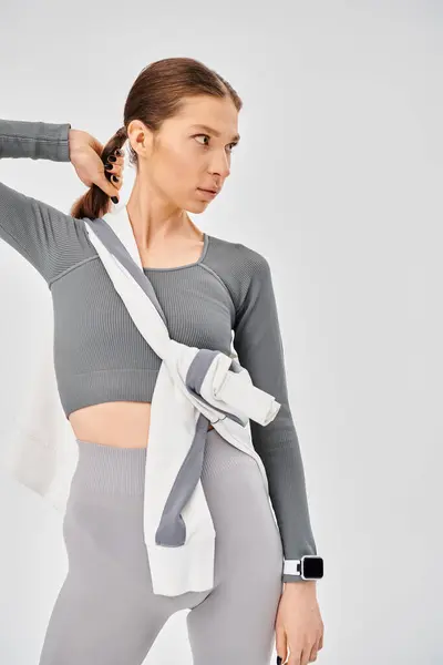 Une jeune femme sportive pose élégamment en haut gris et leggings sur un fond neutre. — Photo de stock
