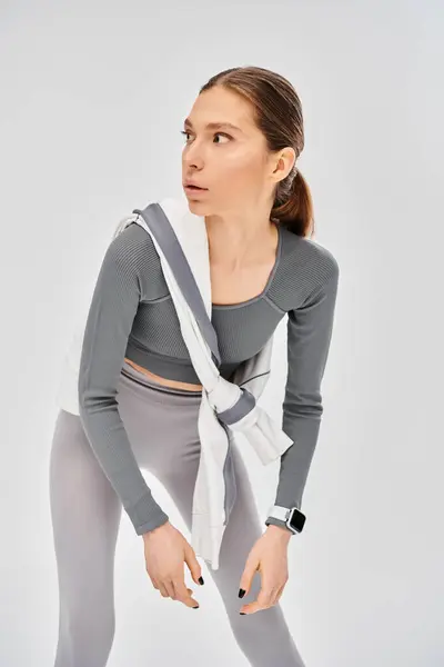 Eine sportliche junge Frau steht selbstbewusst mit einem weißen Schal um den Hals vor grauem Hintergrund.. — Stockfoto