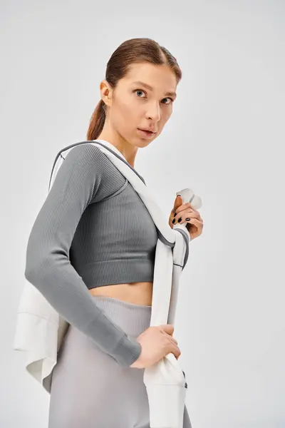 Uma jovem esportiva em um top de sutiã esportivo e leggings, exalando energia e confiança contra um fundo cinza. — Fotografia de Stock