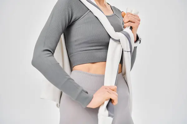 A sporty young woman confidently poses in her gray top and leggings against a backdrop of gray. — Stock Photo