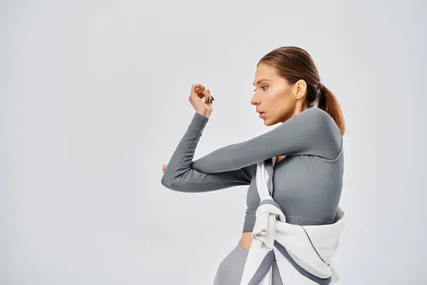 Una giovane donna sportiva con una camicia grigia che lavora su uno sfondo grigio chiaro. — Foto stock