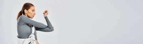 Sportliche junge Frau im grauen Hemd trainiert elegant vor grauem Hintergrund. — Stockfoto
