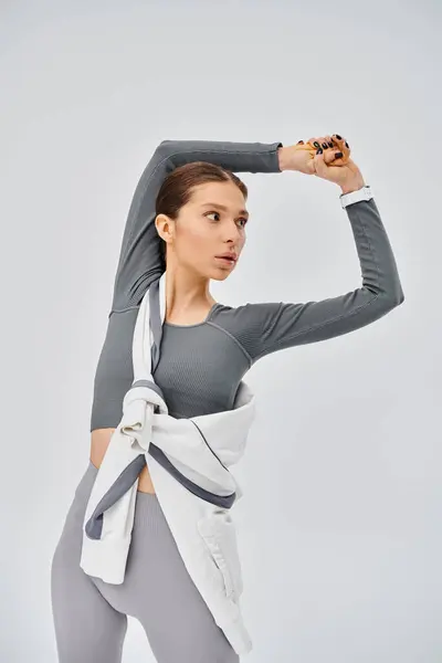 A sporty young woman in grey and white attire striking a pose against a grey background. — Stock Photo