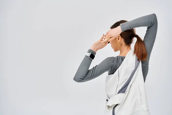 A sporty young woman in active wear sits on a grey background, holding her head in anguish. — Stock Photo