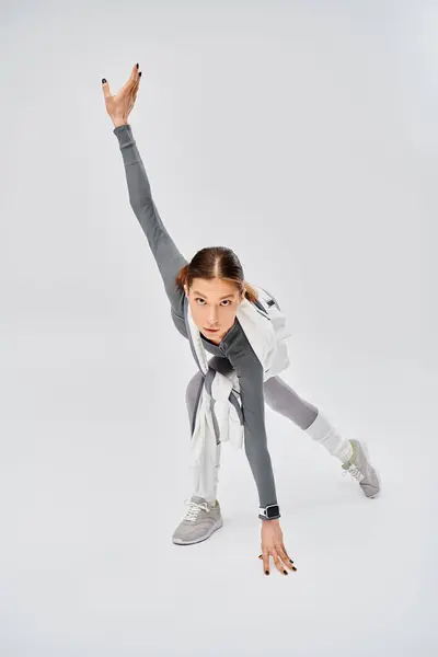 A sporty young woman in active wear dancing gracefully in a studio on a grey background. — Stock Photo