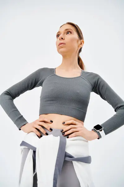 A sporty young woman in active wear confidently stands with hands on hips against a grey background. — Stock Photo