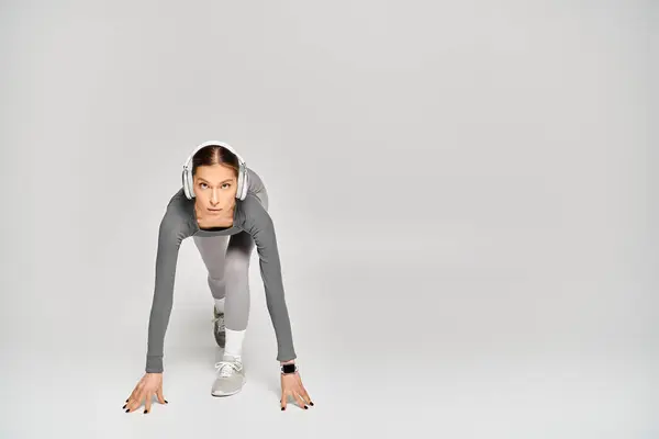 A sporty young woman in active wear showcases her strength by performing a push up with her hands on a grey background. — Stockfoto