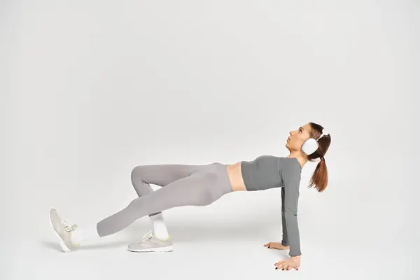 A sporty young woman performs a side plank exercise with grace and strength on a white background. — Stockfoto