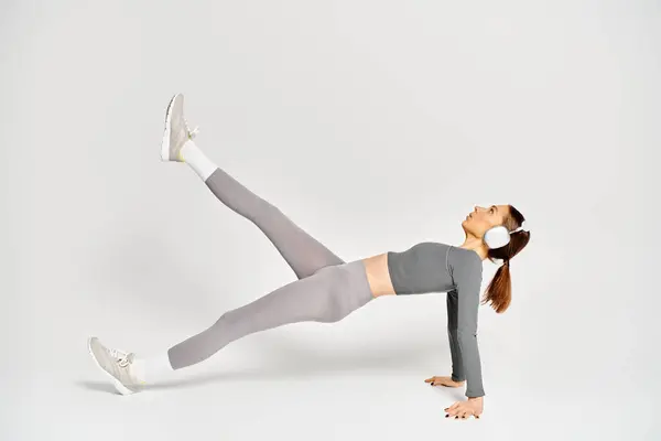 Una joven deportiva en ropa deportiva demostrando un ejercicio de tablón lateral sobre un fondo gris. - foto de stock