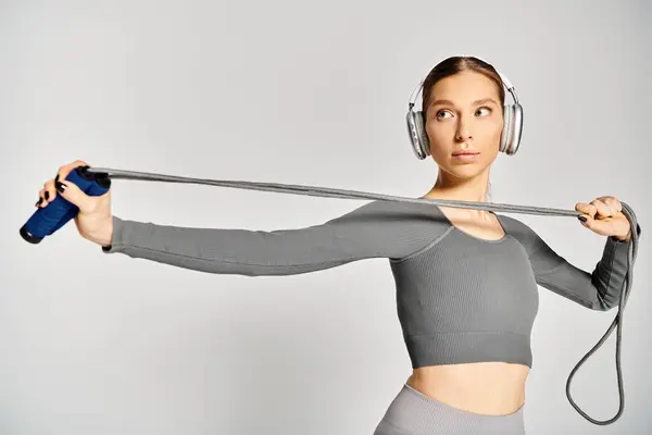 Sportliche junge Frau in aktiver Kleidung hält anmutig ein Springseil, das Kraft und Gleichgewicht verkörpert, mit Kopfhörer auf. — Stockfoto