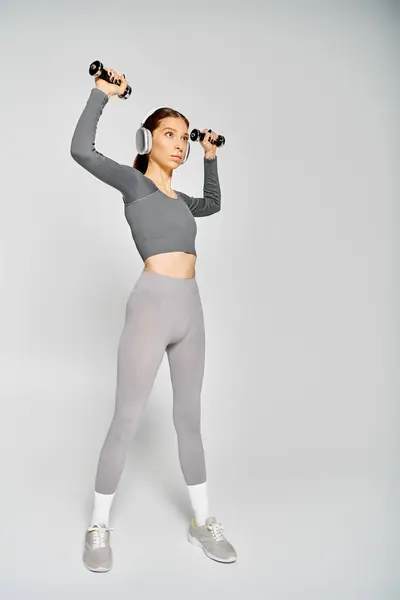 Спортивна молода жінка в активному одязі займається з гантелями на сірому фоні. — стокове фото