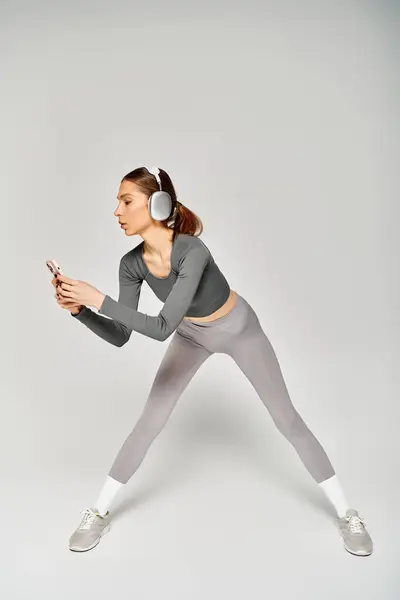 A sporty young woman in gray activewear exudes confidence and grace as she moves on a neutral grey background. — Stock Photo