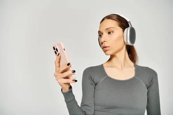 Спортивная девушка в активной одежде слушает музыку в наушниках, держа в руках мобильный телефон. — стоковое фото