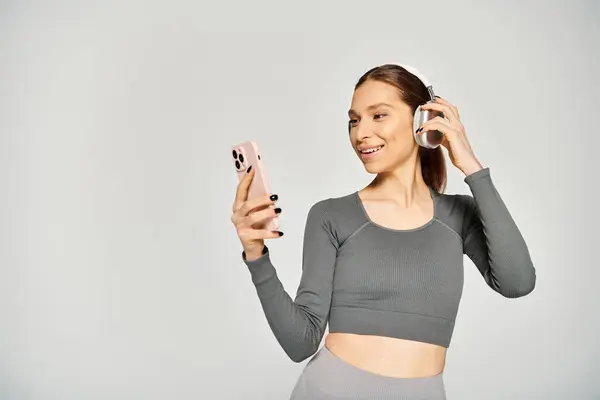 A sporty young woman effortlessly manages a cell phone and headphones. — Stock Photo