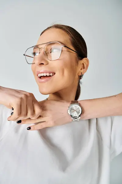 Une jeune femme dans un t-shirt blanc et des lunettes debout sur un fond gris. — Photo de stock