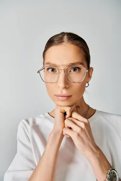 A stylish young woman in a white t-shirt and glasses striking a pose against a grey background. — Stock Photo