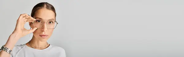 A young woman in a white shirt and glasses poses against a grey background, exuding a sense of sophistication and intelligence. — Stock Photo
