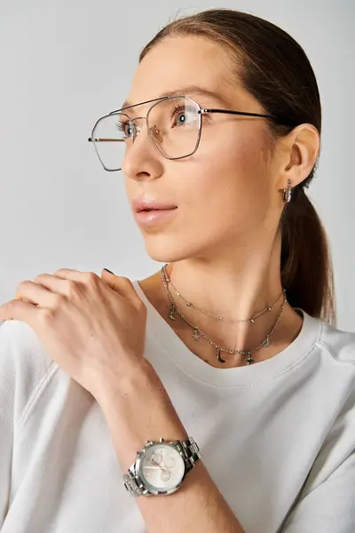 Une jeune femme dégage une élégance moderne dans une chemise blanche, complétée par des lunettes élégantes, sur fond de gris neutre. — Photo de stock