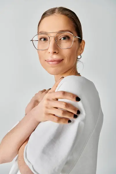 Una joven con gafas y una toalla blanca envuelta sobre sus hombros, capturada en un llamativo retrato sobre un fondo gris. - foto de stock