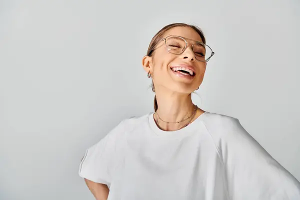 Una giovane donna con gli occhiali travi luminose in una camicia bianca croccante su uno sfondo grigio neutro. — Foto stock