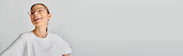 A young woman wearing glasses and a white shirt poses against a grey background, exuding a sense of calm and confidence. — Stock Photo