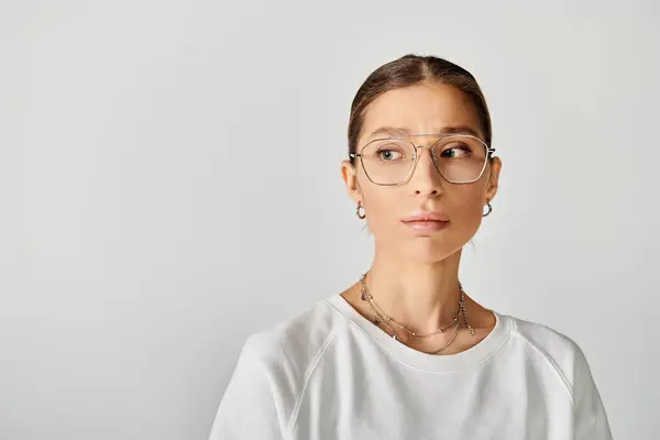 Uma jovem elegante está usando óculos e uma camisa branca contra um fundo cinza. — Fotografia de Stock