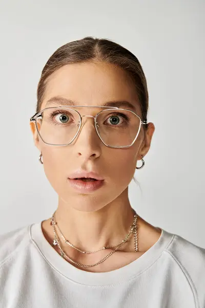 A young woman in glasses wears a surprised expression on a grey background. — Stock Photo