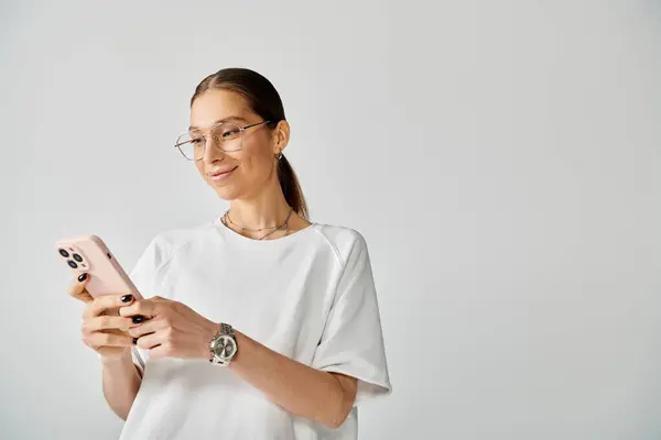 A young woman in glasses holds a cell phone against a grey background. — Stock Photo