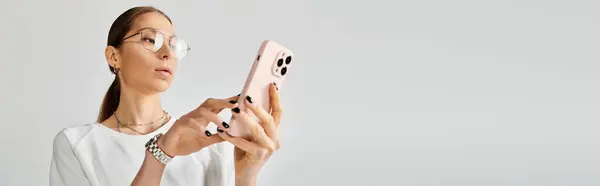 A young woman in a white t-shirt and glasses holding a pink smartphone on a grey background. — Stock Photo