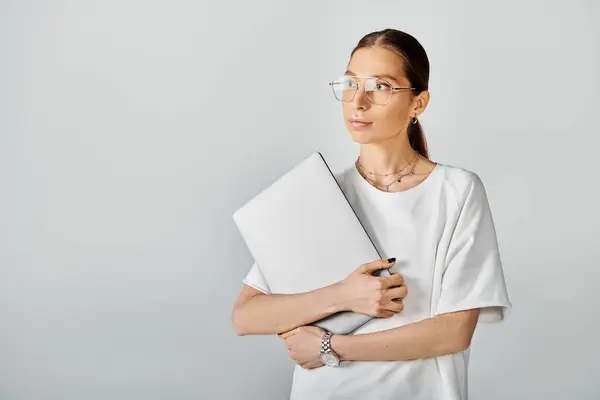 Mujer joven en gafas que sostiene el ordenador portátil, profundamente en el pensamiento, listo para anotar sus ideas e inspiraciones. - foto de stock
