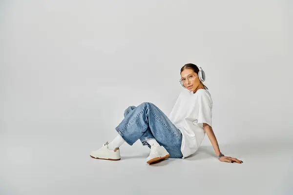 A young woman in white t-shirt and glasses sitting on the ground with her legs crossed. — Stock Photo