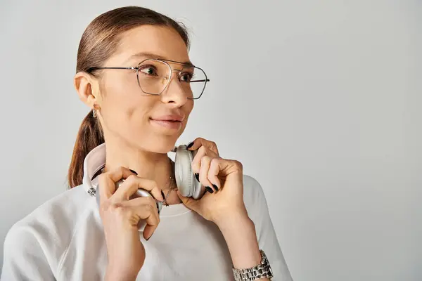 Young woman exudes confidence, wearing glasses and a white t-shirt against a grey background. — Stock Photo