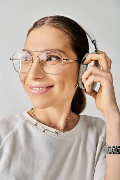 A young woman in a white t-shirt and glasses holding a headset on a grey background. — Stock Photo