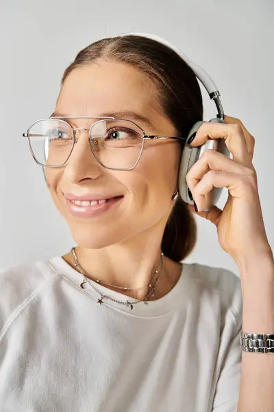Молодая женщина в белой футболке и очках, держащая гарнитуру на сером фоне. — стоковое фото