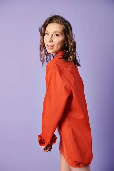 Une jeune femme élégante en chemise orange pose avec confiance sur un fond violet audacieux. — Photo de stock