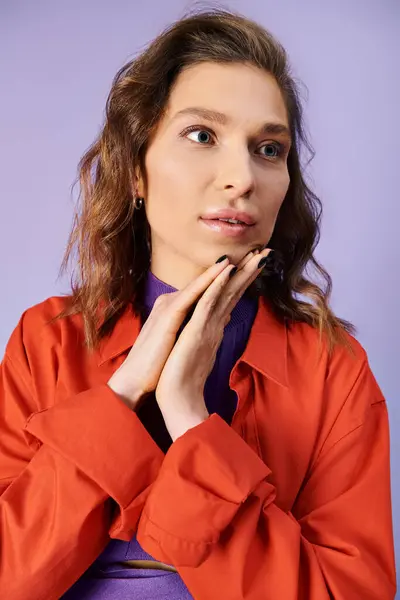 Стильна молода жінка в яскраво-помаранчевій куртці вражає позу на фіолетовому фоні. — стокове фото