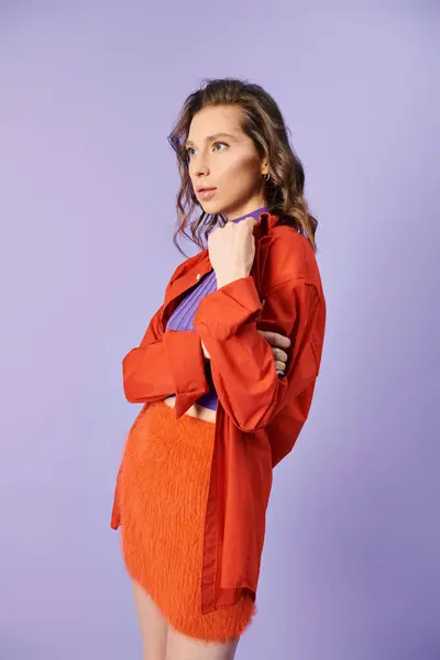Stylish young woman exudes confidence while posing in vibrant orange skirt against purple background. — Stock Photo