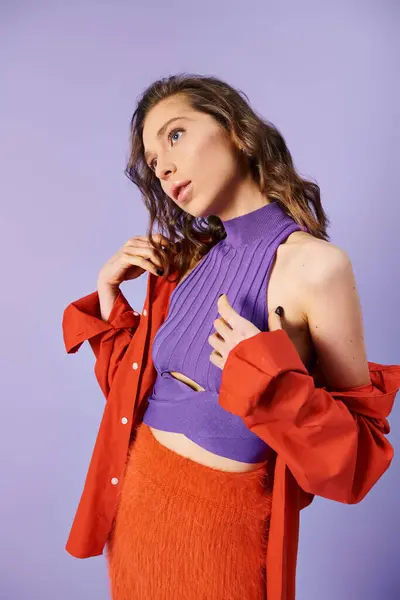 A stylish young woman wears a purple top and vibrant orange skirt, standing out against a purple background. — Stock Photo