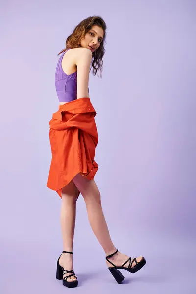Eine stylische junge Frau sticht in einem leuchtend orangefarbenen Rock und lila Oberteil vor passendem Hintergrund hervor.. — Stockfoto