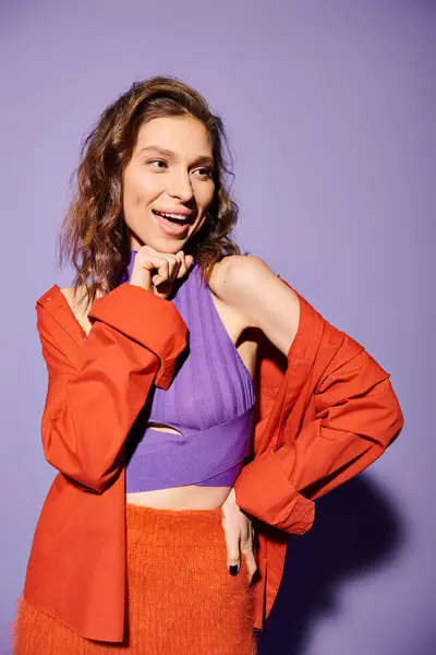 Stylish young woman exudes confidence in a purple top and an orange skirt against a vibrant purple background. — Stock Photo